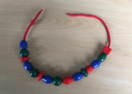 Small coloured beads threaded onto a red piece of string, in the pattern blue, green, red, blue, green, red, etc.