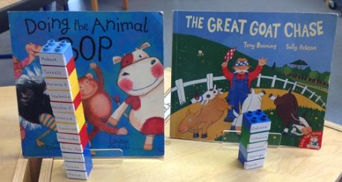 Two children's books are displayed on a table. Each book has a stack of blocks in front of it, and each block has a name written on it.