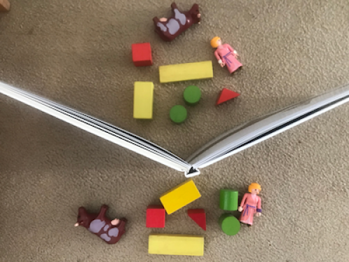 Two identical collections of small toys, either side of an upstanding open book.