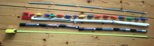 Lines of items arranged end-to-end on the floor. The items are: pencils, toy dinosaurs, rolls of paper, whiteboard pens and a tape measure.