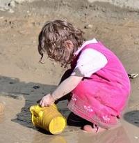 A young girl is scooping some wet sand into a bucket.