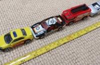 A line of small toy cars with a tape measure stretched out beside them.
