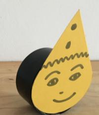 A coffee jar lid with a teardrop-shaped piece of card stuck to it, decorated with a smiling face and a party hat. This is a tocker (explained below).