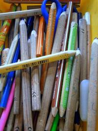 An assortment of coloured pencils, as well as a pair of scissors, are lying in a tray.