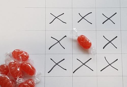 A 3-by-3 grid with a red sweet in the middle square and all other squares marked with crosses.