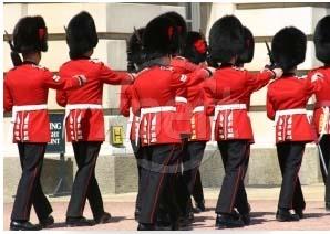 Some soldiers wearing busby hats and red coats are marching in a line towards the right.