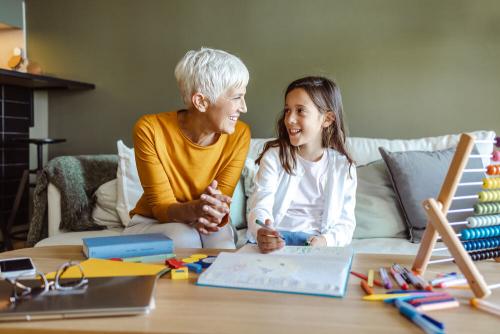 Women and primary school aged girl sitting on a sofa, with a table in front of them with a notebook and lots of maths stationery