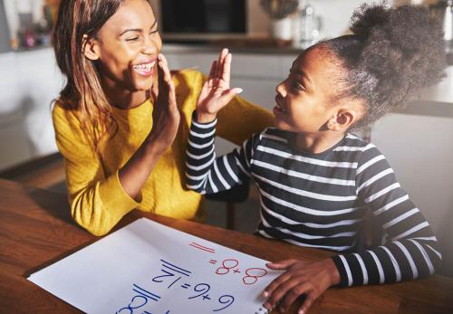 Woman and primary school aged girl high fiving at a table with a notebook