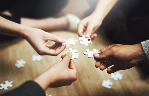 Four peoples' hands holding puzzle pieces that fit together