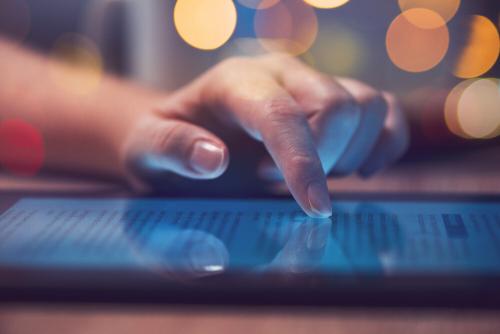 A hand touching the screen of a tablet on a table.
