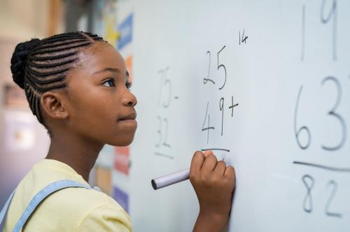Young girl doing column addition and subtraction on a large whiteboard.
