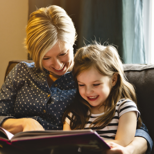A mother and daughter reading a book and smiling.