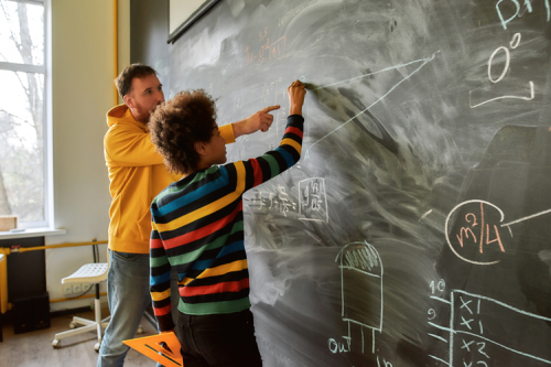 A teacher and student at a blackboard, with the student doing maths.