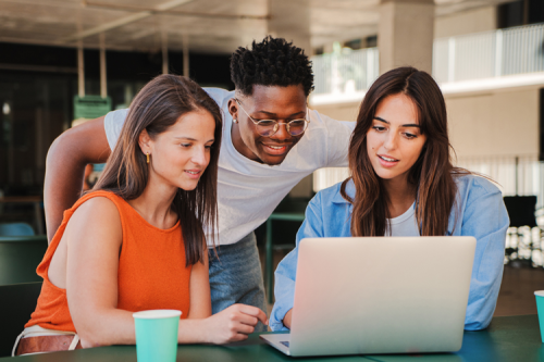 A group of teenagers looking at a laptop and smiling.