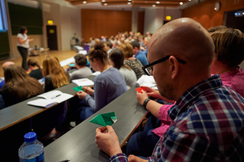 Adults in a lecture theatre, making origami shapes.