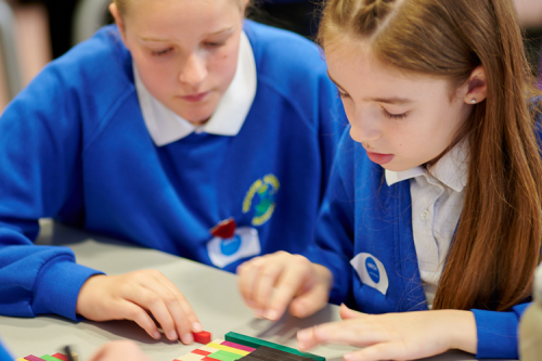 Two girls at a table moving Cuisenaire rods around.