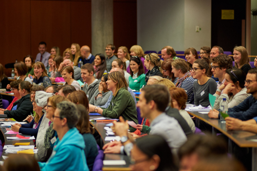 Cheerful teachers in a lecture theatre with coloured paper in front of them.