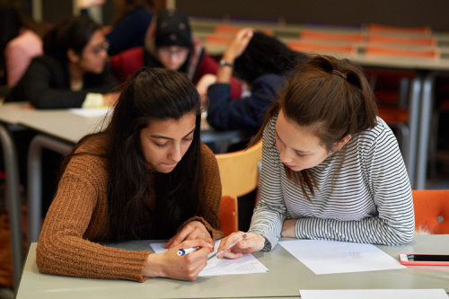 Two teenage girls sitting at a table, discussing their work.